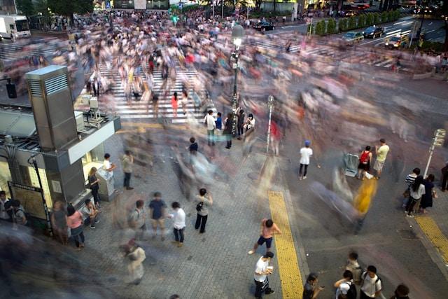 A blurred view of a bustling street filled with numerous pedestrians walking in various directions